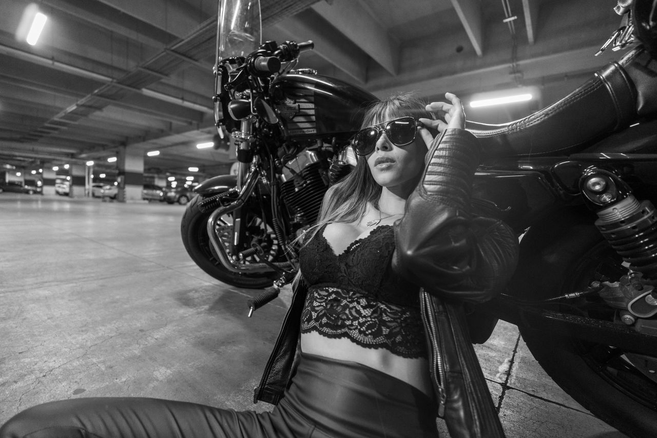 Stylish woman poses with motorcycle in an urban parking garage, exuding glamour and confidence.