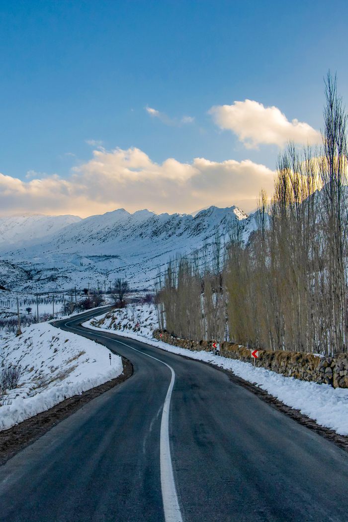 Winding road through snow-covered mountains at sunset, showcasing the beauty of winter landscapes.