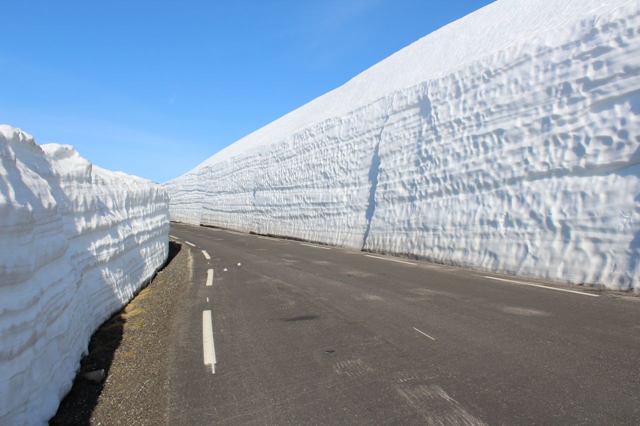 Road lined with tall snow walls under a clear blue sky, showcasing winter's beauty.